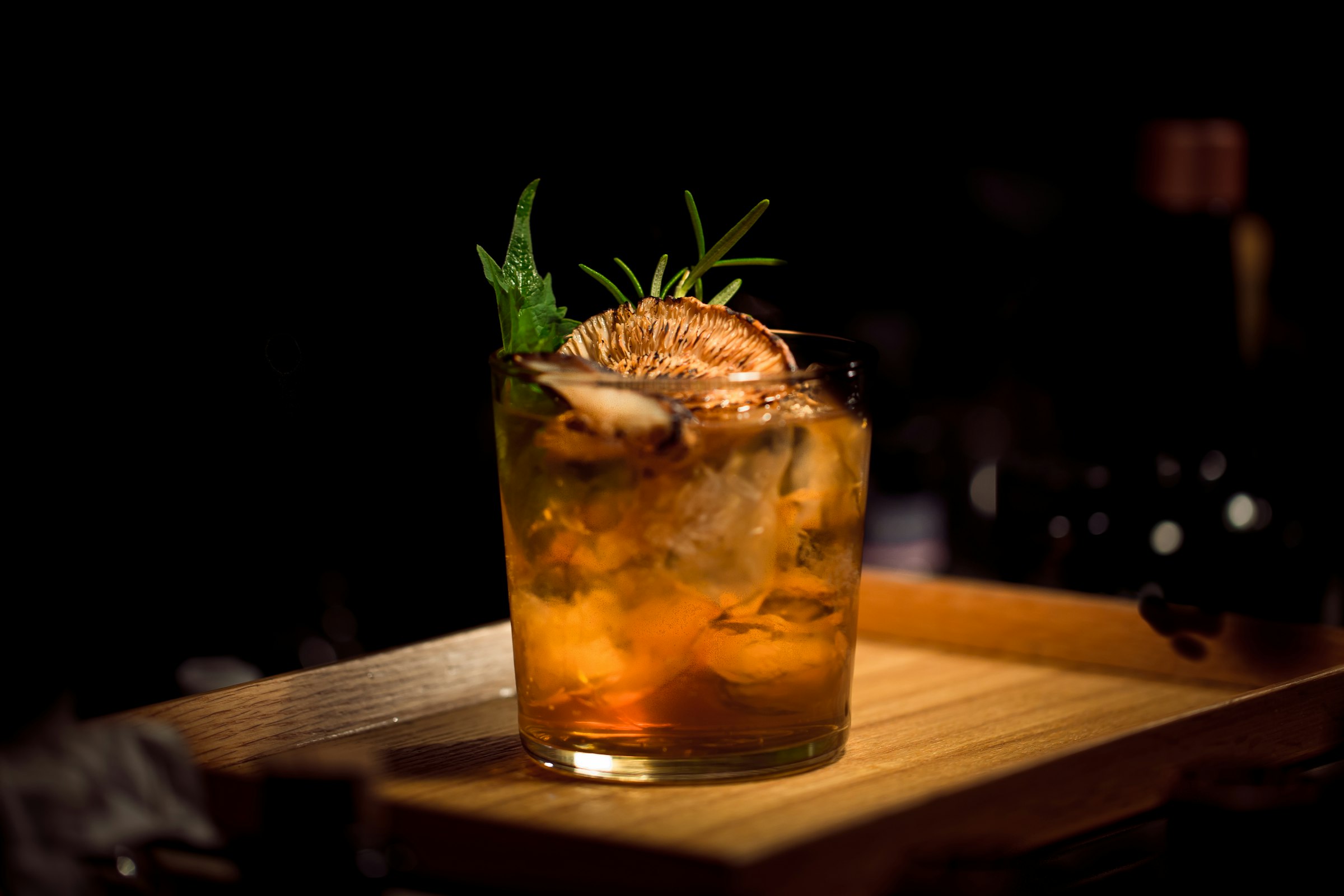 Craft cocktail in low light — amber drink with citrus and herbs